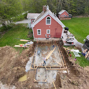 Foundation forms with rebar beside a red farmhouse